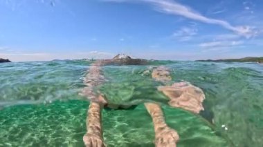 Young woman dives and swims in clear sea water. Girl swimmer in green swimsuit underwater at sea. Half underwater slow-motion shot
