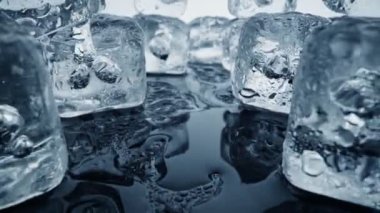 Melted ice cubes close up. Camera moves through ice cubes with water drops over dark background. Wet melted ice cubes with waterdrops. Ice super macro. Slider shot, 4K UHD