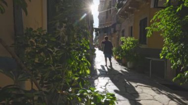 Unrecognizable woman walks along cobbled street between old houses in Kerkyra, Corfu island, Greece. Narrow streets of the old town. Local people in Corfu island. Gimbal slow motion shot 2