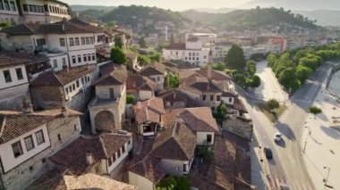 Arnavutluk 'un Berat kentindeki evler, camiler ve minarelerden oluşan kiremitli çatıların üzerinden uçuyorlar. Arnavutluk 'un en güzel kenti Berat' taki muhteşem Osmanlı binaları. Hava görüntüsü, 4K