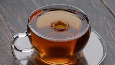 Damlacık altın çaya dökülüyor. Kokulu siyah çay damlaları çay ile şeffaf fincana düşer. Yavaş çekim çay sıçraması.