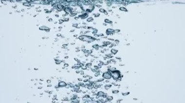 Suda hava kabarcıkları. Beyaz zemin üzerinde maden suyundaki baloncukların yavaş çekim görüntüleri. Su kaynıyor.