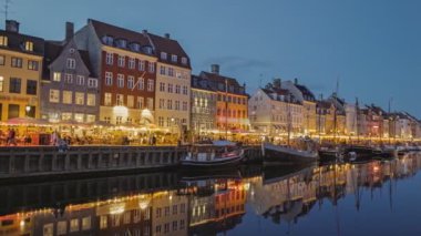 Nyhavn Kanalı New Harbour 'un renkli evleri ve Kopenhag' da yelkenli tekneleri ile akşam çekimleri. 4K HDR çekimi. İnsanlar kanal boyunca yürür, Kopenhag, Danimarka