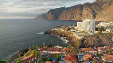 Aerial view of Los Gigantes restort on Tenerife Canary island. Flying over magnificent hotels, villas and natural pool on the ocean - rocks in sunset light in the background. Canary islands, Spain