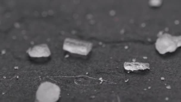 黒い石の表面に落ちる塩結晶のスーパーマクロショット 高倍率の塩粒のスライダーショット — ストック動画