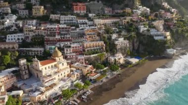 Renkli evlerin, kilisenin ve plajların üzerinde turkuaz suyla uçuyor. Positano köyü, İtalya. Amalfi sahilinin ünlü turistik beldesi, Positano. UHD, 4K