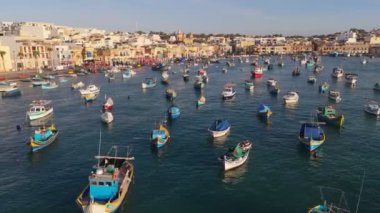 Marsaxlokk, Malta 'daki balıkçı kasabasının limanında renkli teknelerin üzerinde uçuyor. Gün doğumunda Marsaxlokk 'un hava görüntüsü