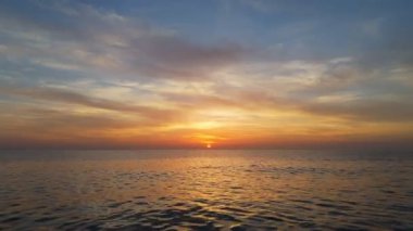 Okyanusun üzerinde destansı gün batımı. Güneşin havadan görüntüsü ufuktan aşağı iniyor. Suyun üzerinde parlak turuncu ve sarı gün batımı