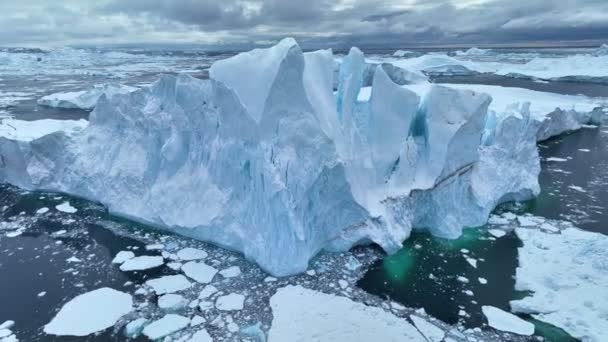グリーンランドのイルリサット近くの巨大な氷山の上を飛ぶ 氷山の断片が分裂して水に落ちる 地球温暖化と気候変動のコンセプト — ストック動画