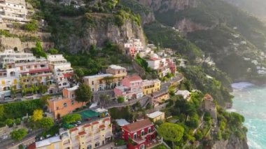 Denizin üzerindeki uçurumun üzerindeki renkli evlerin üzerinde turkuaz suyla uçuyor. Positano köyü, İtalya. Amalfi sahilinin ünlü turistik beldesi, Positano. Hava görüntüsü, UHD, 4K