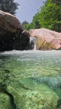 Yarısı su altında, hızlı dağ akıntısı ve kristal berrak su. Nehir taşların arasından akar ve küçük şelaleler ve banyolar oluşturur, VERTICAL VIDEO 