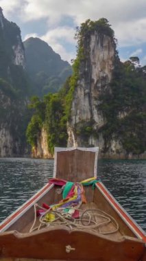 Tayland 'daki Khao Sok Ulusal Parkı' ndaki Cheow Lan gölünde tekne gezisi. Meşhur Üç Kız Kardeş Karst oluşumları uzaklarda görülür. Tayland 'ın muhteşem doğası. Dikey çekim