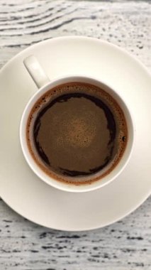 Sıcak siyah kahve karıştırıldıktan sonra beyaz bardakta dönüyor. Kahverengi ve turuncu, hava kabarcıklı. Üst aşağı dikey çekim