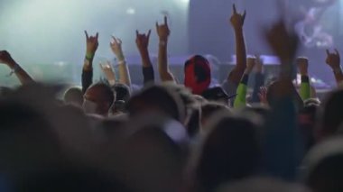 Hayranlar rock konserinde dans edip zıplıyorlar. Parlak sahne ışıkları önünde konser kalabalığının siluetleri. Yavaş çekim, 4K 
