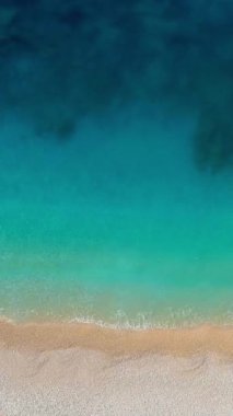 Mükemmel turkuaz plajın havadan aşağı manzarası. Açık mavi deniz suyu - mükemmel bir yaz tatili. Beyaz kumla boş kumsalın üzerinde uçmak. Dikey Video