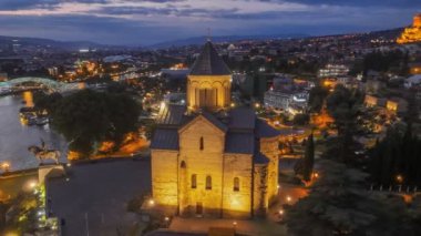 Şehir ışıklarıyla Tiflis 'in akşam manzarası. Tiflis şehir merkezinde Metekhi 'nin Bakire Meryem Varsayım Kilisesi' nin etrafında uçuyor. Arkaplanda gün batımı gökyüzü