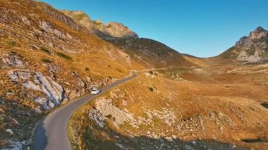 Dağlarda manzaralı yılan yolu boyunca giden beyaz bir araba. Arabayla yaz macerası. Havadan yüksek kalite İHA atışı