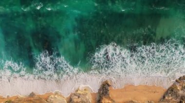 Okyanus sörfü ve kayalarla dolu kumlu sahilin yukarıdan görünüşü. Köpüklü güçlü okyanus dalgaları, Bali, Uluwatu yakınlarında.