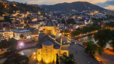 Tiflis şehir merkezinde Metekhi 'nin Bakire Meryem Varsayım Kilisesi' nin etrafında uçuyor. Şehir ışıklarıyla Tiflis, Georgia 'nın akşam manzarası. Arkaplanda gün batımı gökyüzü