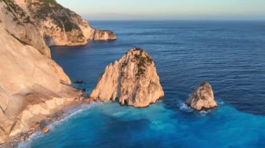 Güneş Yunanistan 'ın İyonya Denizi' ndeki Zakynthos adasındaki tenha sahilde batarken, kıyı kayalıklarının canlı mavi sularla buluşmasının nefes kesici güzelliğine tanık olun. Uçurum turkuaz gölle çevrili.