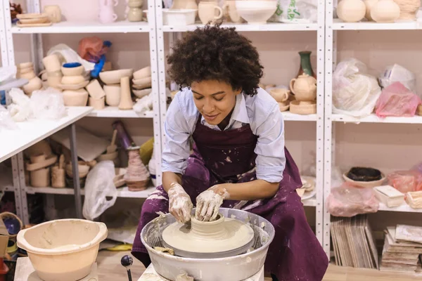 Creative afro american young woman molding clay on pottery wheel. Workshop in ceramic studio. Female artist.