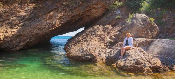 身穿白衬衫 头戴白帽的女人 坐在洞口旁边的岩石上 享受暑假 休闲的生活方式度假的概念阳光灿烂 — 图库照片