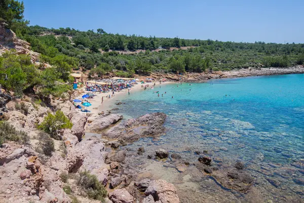 Rahatlatıcı insanlar, turkuaz deniz ve mavi gökyüzü çam ormanlarıyla çevrili bir kumsalda cennet manzarası yaratır. Resimli bir Akdeniz tatil köyünün sakin körfezi.