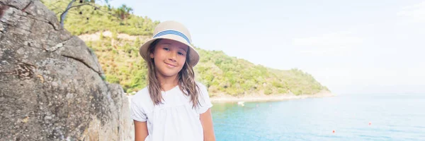 岩の海岸に帽子をかぶったかわいい幸せな女の子の肖像画 背景に美しい夏の海 — ストック写真