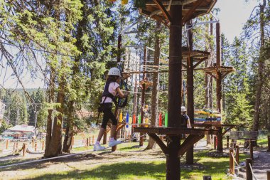 Bir yaz kampı sırasında, gür bir ormanın göbeğindeki heyecan verici ağaç tepesi macera parkında korkusuz genç kız..