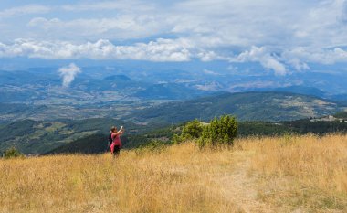 Yazın doğa manzarasından zevk alan bir kadın yürüyüşçü, çarpıcı bir çevreyle akıllı telefonuyla fotoğraf çekiyor..