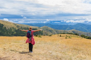 Kollarını uzatmış mutlu bir kadın dağın zirvesinde dinleniyor, büyüleyici yaz manzarası..