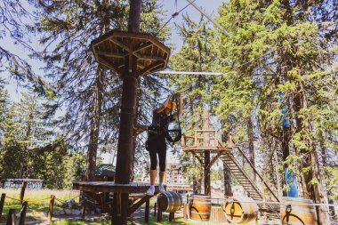 Kız, lunaparktaki bir ormanda koruyucu giysiler giyerek zorlu bir halat kursundan geçiyor..