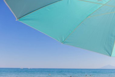 Turkuaz Sahili Şemsiyesi Deniz kenarında güneşli bir yaz günü tatil, dinlenme ve yaz teması için ideal.