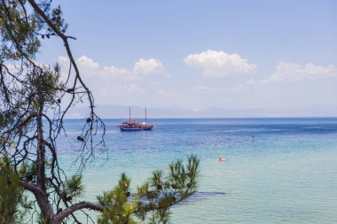 Renkli bir yelkenlinin kristal berrak sularda yüzdüğü güzel Akdeniz sahili.
