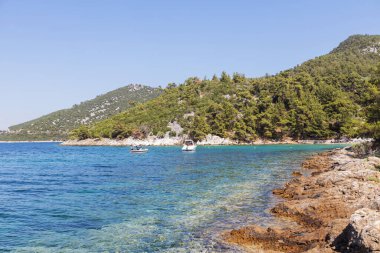 Akdeniz 'in sakin sularına bakan güneşli kayalık plajlarda yüzen tekneler var..