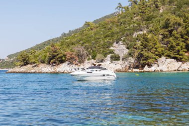 Serin, berrak bir körfeze demirlemiş parlak, kayalık tepelerle çevrili beyaz bir yat..