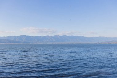Doirani Gölü 'nün sakin sahnesi, sakin suları uzak dağ sıraları ve açık mavi gökyüzü tarafından çerçevelenen ufka kadar uzanıyor.