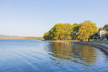 Doiran Gölü 'nün kıyısında, sakin suların günbatımının ılık ışığını yansıttığı engebeli bir göl yolu. Kuzey Makedonya