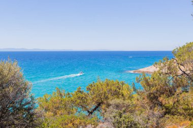 Yunanistan 'ın kayalık kıyı şeridi boyunca canlı turkuaz sularıyla küçük bir tekne süzülüyor, mükemmel yaz atmosferleri var..