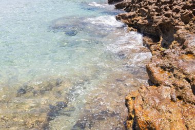 Kristal berrak sular, Yunanistan 'da bir plajın kıyısındaki kayalık oluşumları nazikçe kaplıyor.