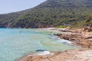 Yunanistan 'da kristal berraklığında suları olan kayalık bir sahil. Engebeli kıyı şeridi sakin ve şeffaf denizle güzel bir tezat oluşturuyor. Rahatlamak için ideal bir yer sunuyor..