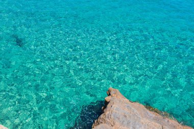 Kristal berrak turkuaz sular parlak güneşin altında parlayarak, Yunanistan 'ın güzel bir sahil şeridinin kayalık kıyılarını ortaya çıkarıyor.