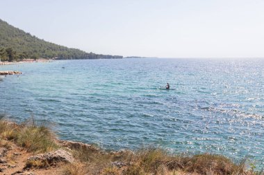 Serin, mavi sularda güneşli bir günün tadını çıkaran kaykaycı yemyeşil sularla çevrili ve kıyı boyunca uzak plajlarda yaşayan.