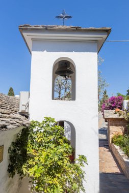 Haçlı beyaz çan kulesi, canlı yeşillik ve güneşli bir günde sakin bir manastır bahçesinde çiçekler..