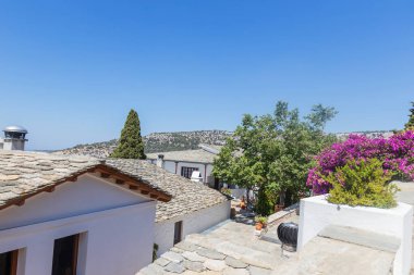 Yunanistan 'ın Thassos kentinde çiçek açan bougainvillea ve geleneksel taş çatılara sahip huzurlu manastır avlusu.