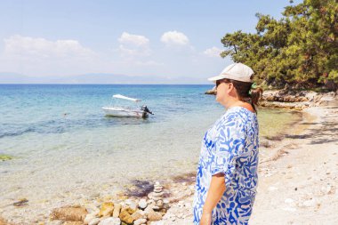 Kadın kayalık bir sahilden berrak mavi denizin manzarasını seviyor..