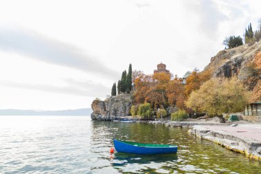 Ortodoks bir kilise olan Kaneo 'daki Aziz John Kilisesi' nin sakin sulara tekneyle bakan bir uçurumun üzerinde durduğu Ohri Gölü manzarası. Renkli sonbahar yaprakları sahneye biraz sıcaklık katıyor..