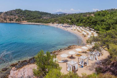 Güneşli şezlonglar, şemsiyeler ve kristal berrak turkuaz sularla sakin sahil sahnesi, Yunanistan 'da rahatlatıcı bir yaz tatili için mükemmel..