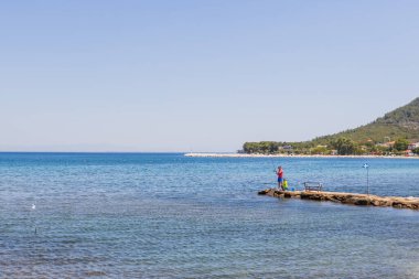 Aile sahilde bir günün tadını çıkarıyor. Bir baba ve çocuk küçük bir rıhtımda balık tutuyor..