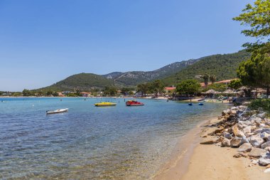 Kristal berraklığında turkuaz suları, kumlu bir plajı ve yemyeşil tepeleri olan görkemli sahil manzarası..